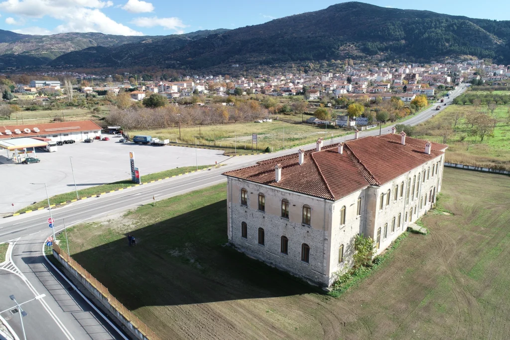 Φωτογραφία του τουρκικού σχολείου, ενός κτηρίου της ύστερης οθωμανικής περιόδου, το οποίο βρίσκεται στη βόρεια είσοδο της σύγχρονης πόλης των Σερβίων. Στο βάθος στης φωτογραφίας διακρίνεται η σύχγρονη πόλη των Σερβίων.